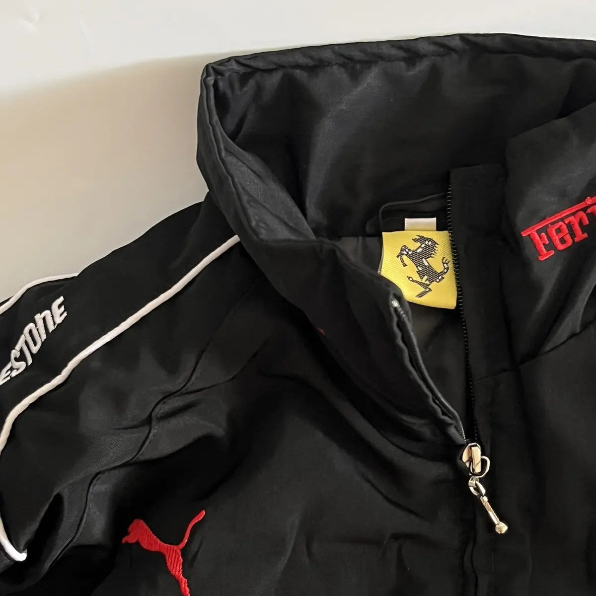 Black jacket with various logos including Ferrari, Puma, and Shell on a light background
